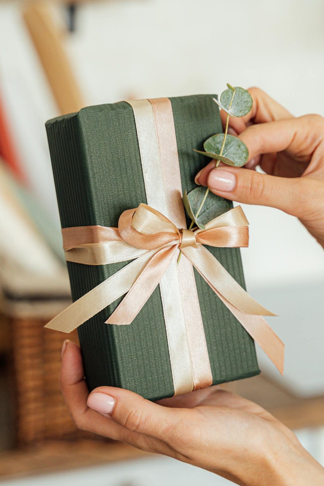 Close-up of hands holding a beautifully wrapped gift box with a ribbon and greenery accent.