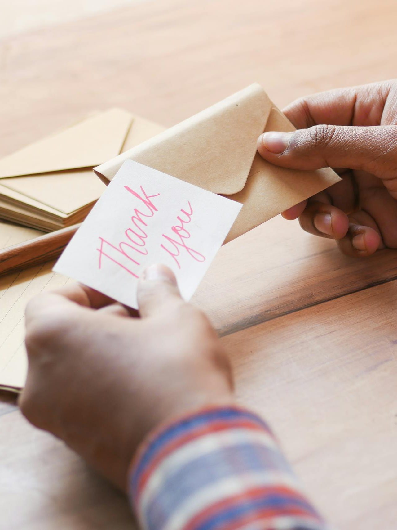 Close-up of hands holding a thank you note in an envelope on a table.